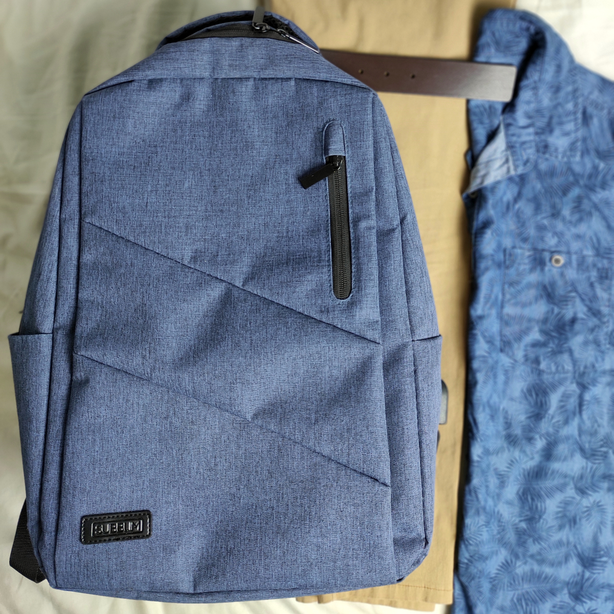mochila azul para portatil subblim con pantalon camel de pinzas y camisa azul tejano de manga corta